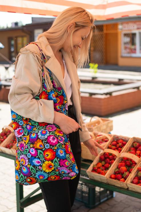 kobieta wybiera truskawki mając czarną łowicką torbę w kwiaty