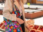 woman picks strawberries while wearing a black folk floral bag